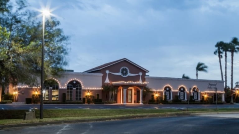 Illuminated brick church building at dusk with arched windows, bell tower, palm trees, and manicured lawn