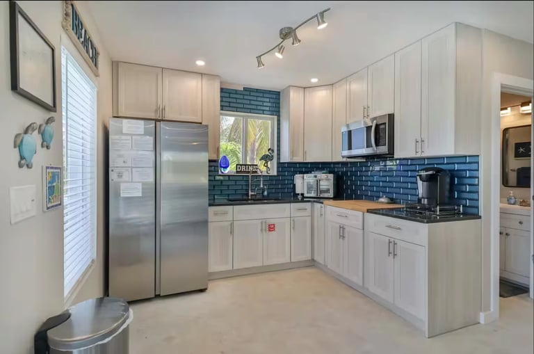 Modern kitchen with white cabinets, stainless steel appliances, blue tile backsplash, and window above sink